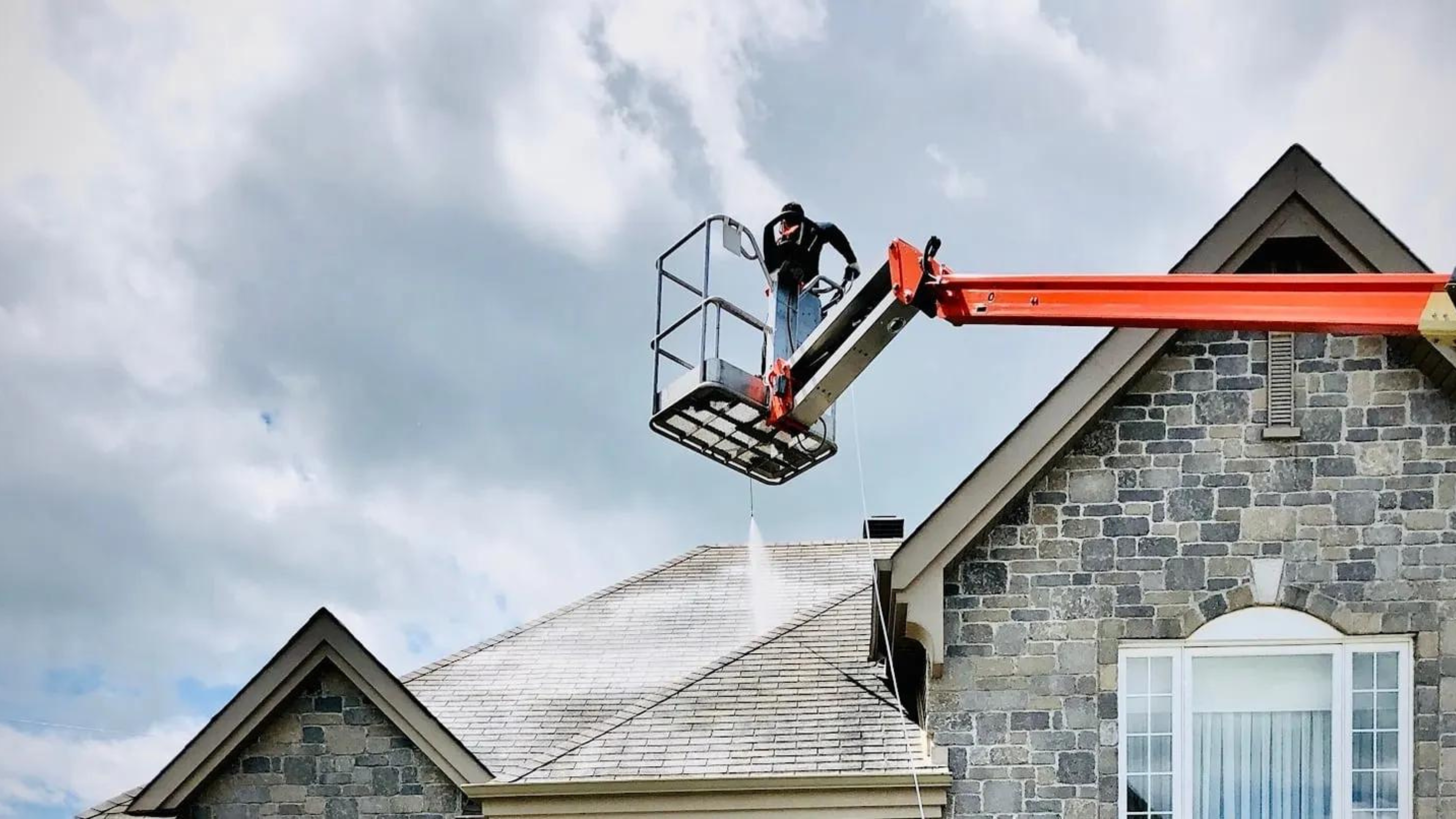 Contractor in a boom lift applying GoNano treatment to a two-story residential roof