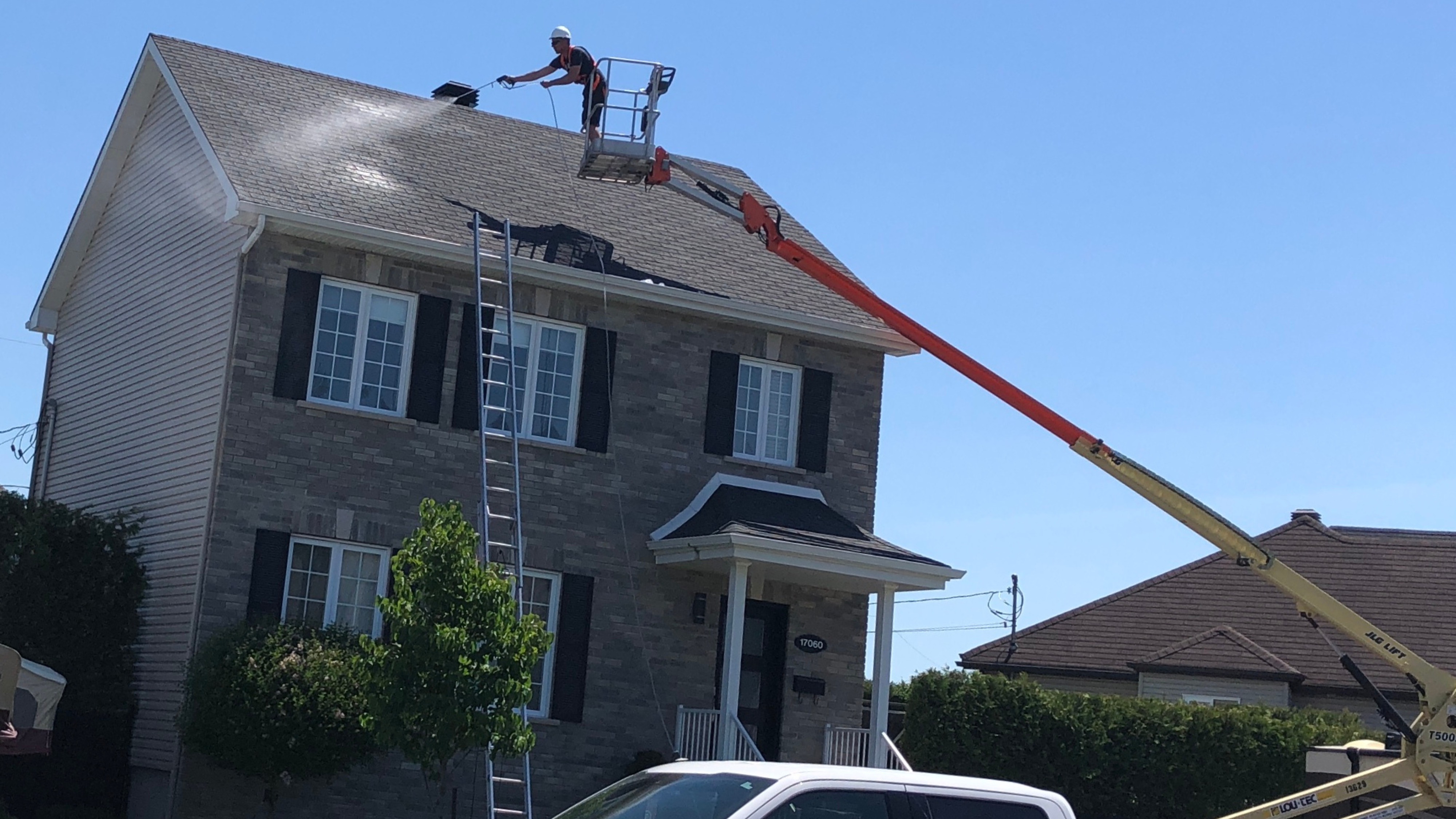 Contractor applying GoNano roof treatment to a residential home using a boom lift on a clear day